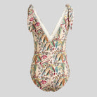 A one-piece swimsuit with a complex multicolor paisley and floral print on a cream base, featuring a deep V-neckline with white trim and tie-shoulder straps, shown against a solid gray background.